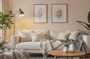 Cozy modern living room with a beige sofa, layered cushions, throw blanket, wooden coffee table, floor lamp, indoor plants, and framed wall art. Warm and inviting atmosphere.