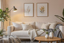 Cozy modern living room with a beige sofa, layered cushions, throw blanket, wooden coffee table, floor lamp, indoor plants, and framed wall art. Warm and inviting atmosphere.