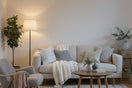 "Cozy small living room with a light sofa, layered cushions, wooden coffee table, floor lamp, and green plants, styled in Scandinavian design to maximize limited space.